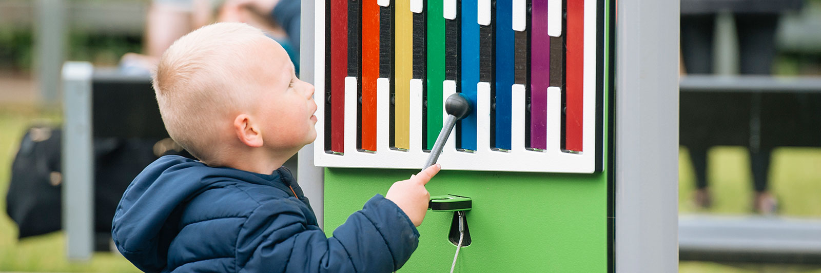 a young boy in a hat and gloves, stands in a snowy playground speaking into a talk tube